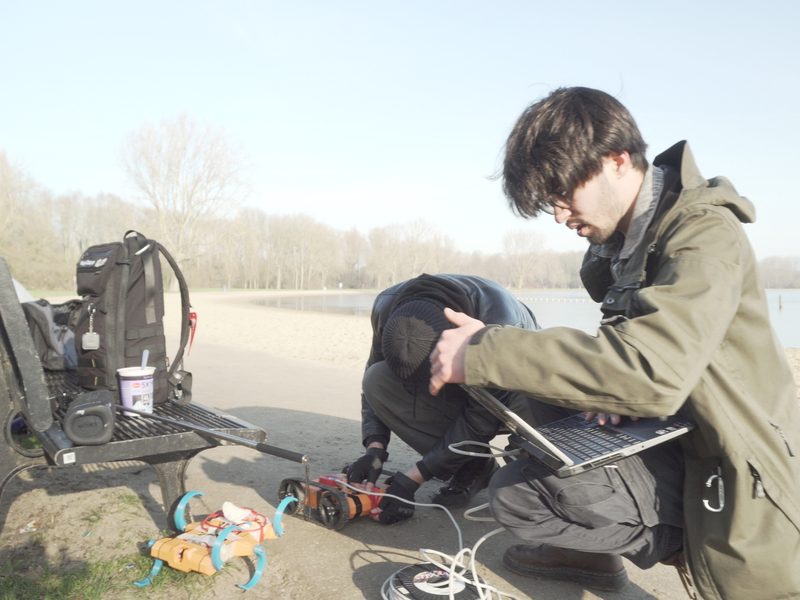 A UNAMIQ engineer crouched beside the ground vehicle during a field test by the water
